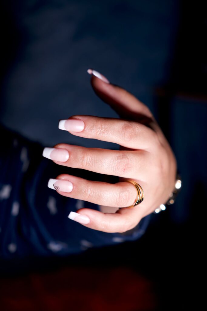 Hand with a clean French manicure wearing gold rings